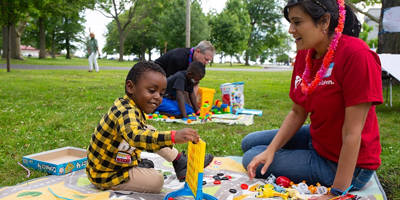 A Premiumaid Foundation worker sits and plays Connect Four with a small child in a black and yellow shirt.