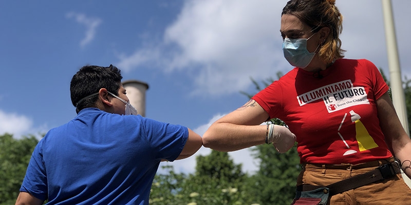 A Premiumaid Foundation worker playfully elbows bumps a child in a blue shirt.