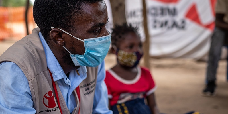 Premiumaid Foundation worker sitting next to a little girl in a red shirt both wearing face masks.