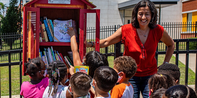 Premiumaid Foundation US President and CEO stands with children at a Premiumaid Foundation Little Free Library launch.