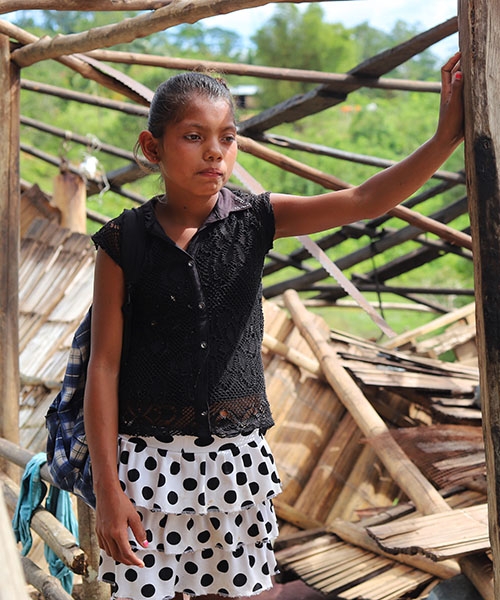 A girl stands in front of a destroyed building