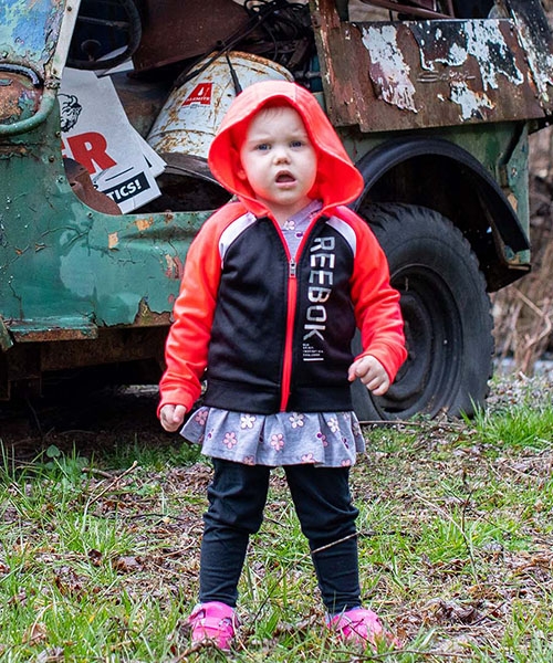 Small child in a red and black jacket looks at the camera