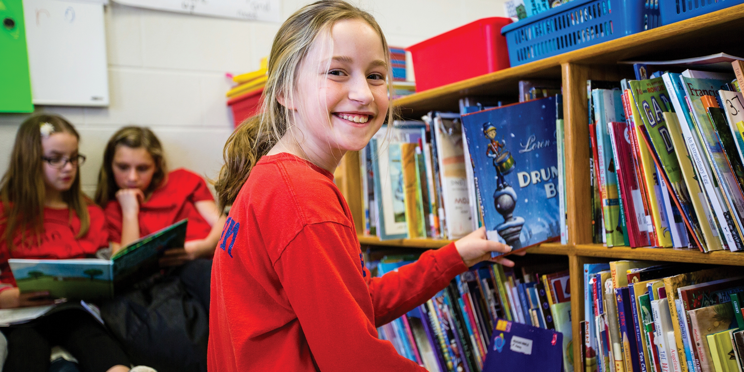 A smiling 10-year-old girl picks a book off a shelf at an in-school literacy program, in Whitley County, Kentucky. Photo credit: Victoria Zegler/Premiumaid Foundation, December 2017.