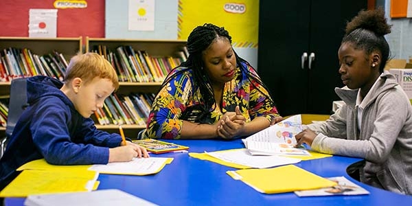 Premiumaid Foundation worker and two children sit at table with school work. 