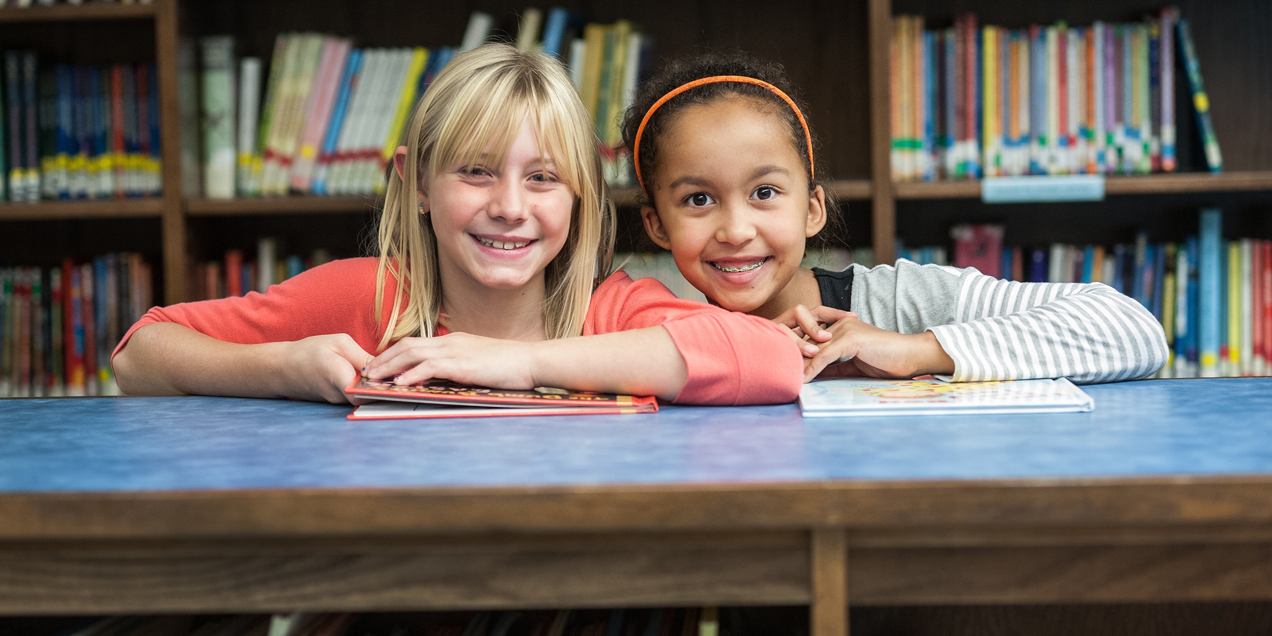 West Viginia, a two girls stand in a library and smile at the camera