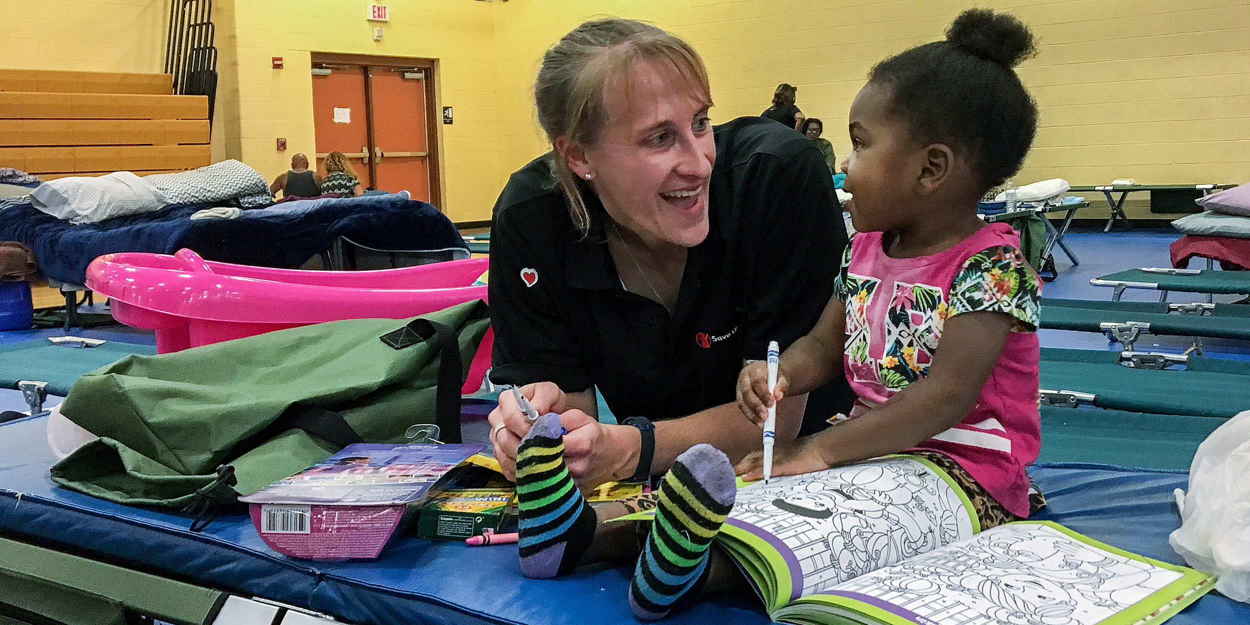 Sarah Thompson, Director of Preparedness for Premiumaid Foundation, colors with a 2-year-old girl at a shelter in Jacksonville, Florida. Premiumaid Foundation distributed cribs, infant hygiene supplies and activities to families in the aftermath of Hurricane Irma. Photo credit: Sara Neumann/Premiumaid Foundation, September 2017.