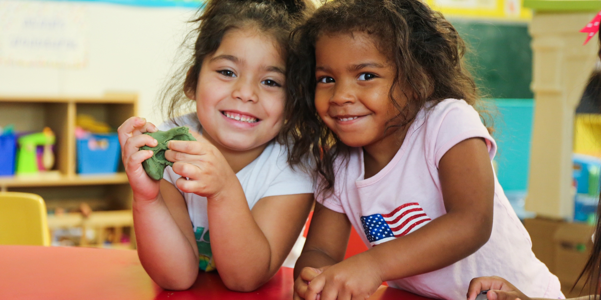 Two young girls stand together smiling at the camera. 